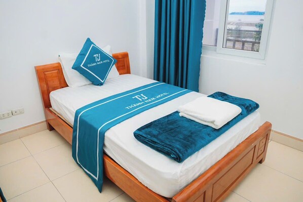 A neatly made bed with a blue bedspread and pillow, a white blanket, and a blue towel. - Thanh Nam Hotel Quan Lan By Bay Luxury (Van Don)