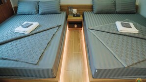 Ein Zimmer mit zwei Betten, jeweils mit einem Kissen und einem zusammengeklappten Handtuch. Ein Nachttisch mit einer Lampe und ein kleiner Tisch zwischen den Betten.