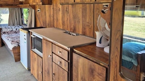 Interni di un camper compatto con mobili in legno, angolo cottura, un letto e un ampio specchio.