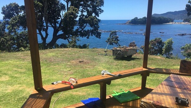 Un patio in legno con tavoli da picnic, una zona verde e vista sul mare e sulle colline.