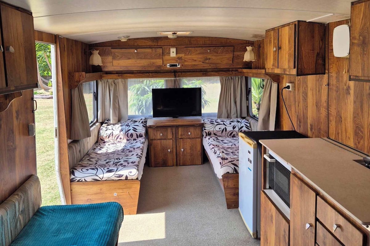 Ein kompaktes Wohnmobil-Interieur mit einer Sitzecke, einem Bett, einem Fernseher und Holzschränken.