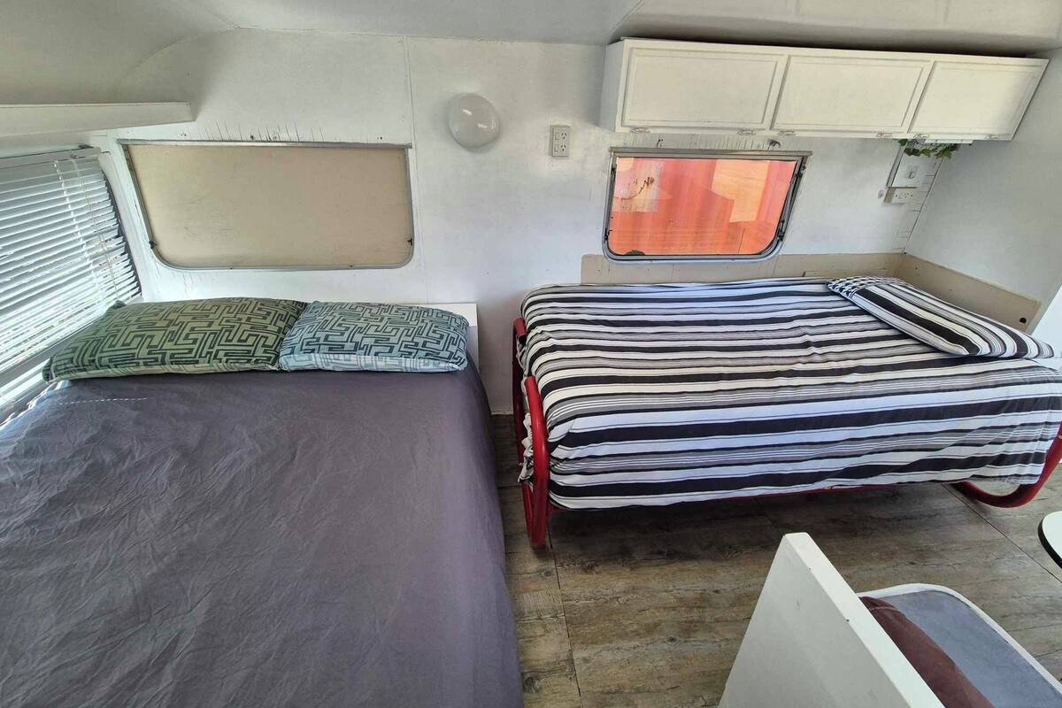 Ein kompaktes Wohnmobil-Interieur mit zwei Betten, einem Fenster und einer kleinen Küchenzeile.
