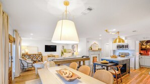 Eine moderne Küche mit weißen Schränken, eine Essecke mit Holztisch und eine große Pendelleuchte.