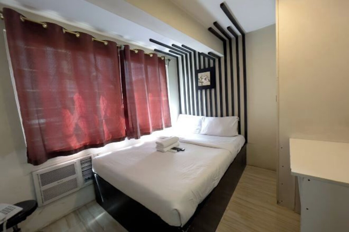 A hotel room with a bed, a desk, and a window with curtains.
