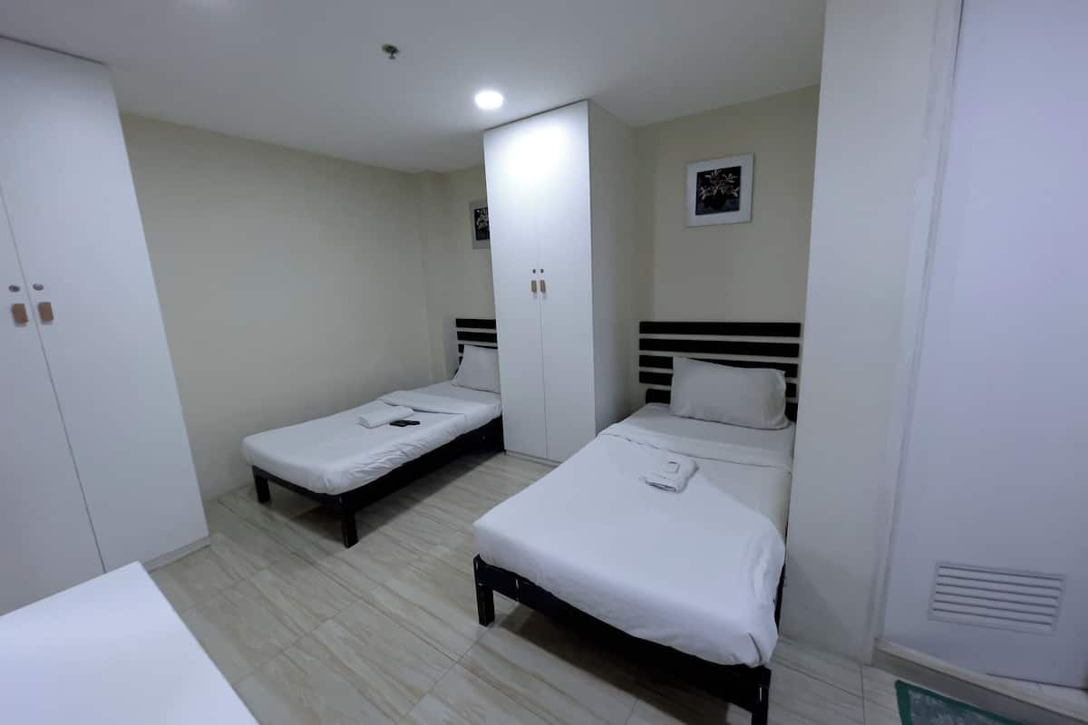 Une chambre d’hôtel avec deux lits simples, une armoire et une petite table de chevet.