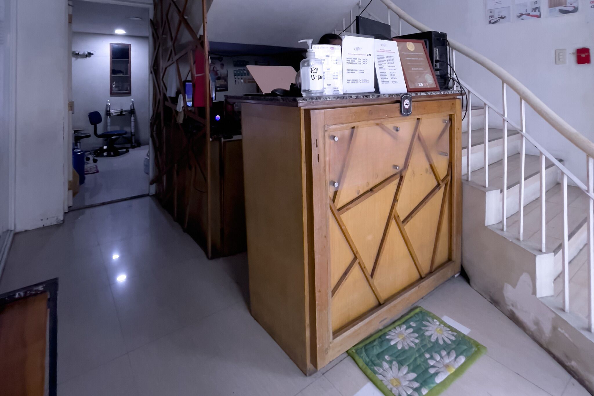 A hallway with a wooden cabinet, a green mat, and a staircase with white railings.