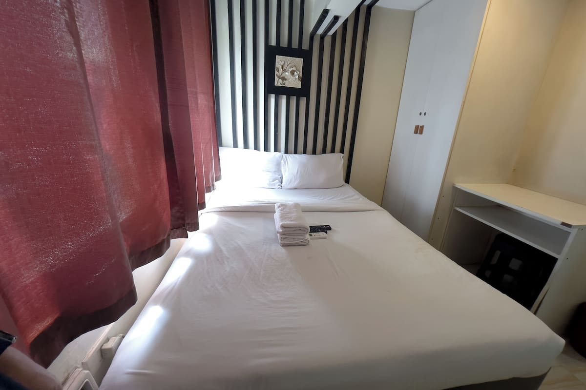 Une chambre d’hôtel avec un lit bien fait, une petite table de chevet et une étagère fixée au mur.