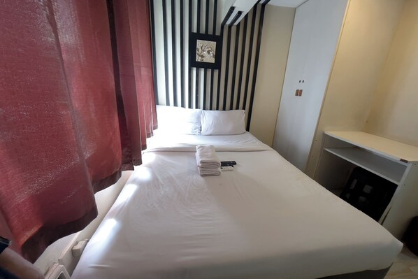 A hotel room with a neatly made bed, a small bedside table, and a wall-mounted shelf. - Jardin Oriental Suites Ubelt Manila (Manila)