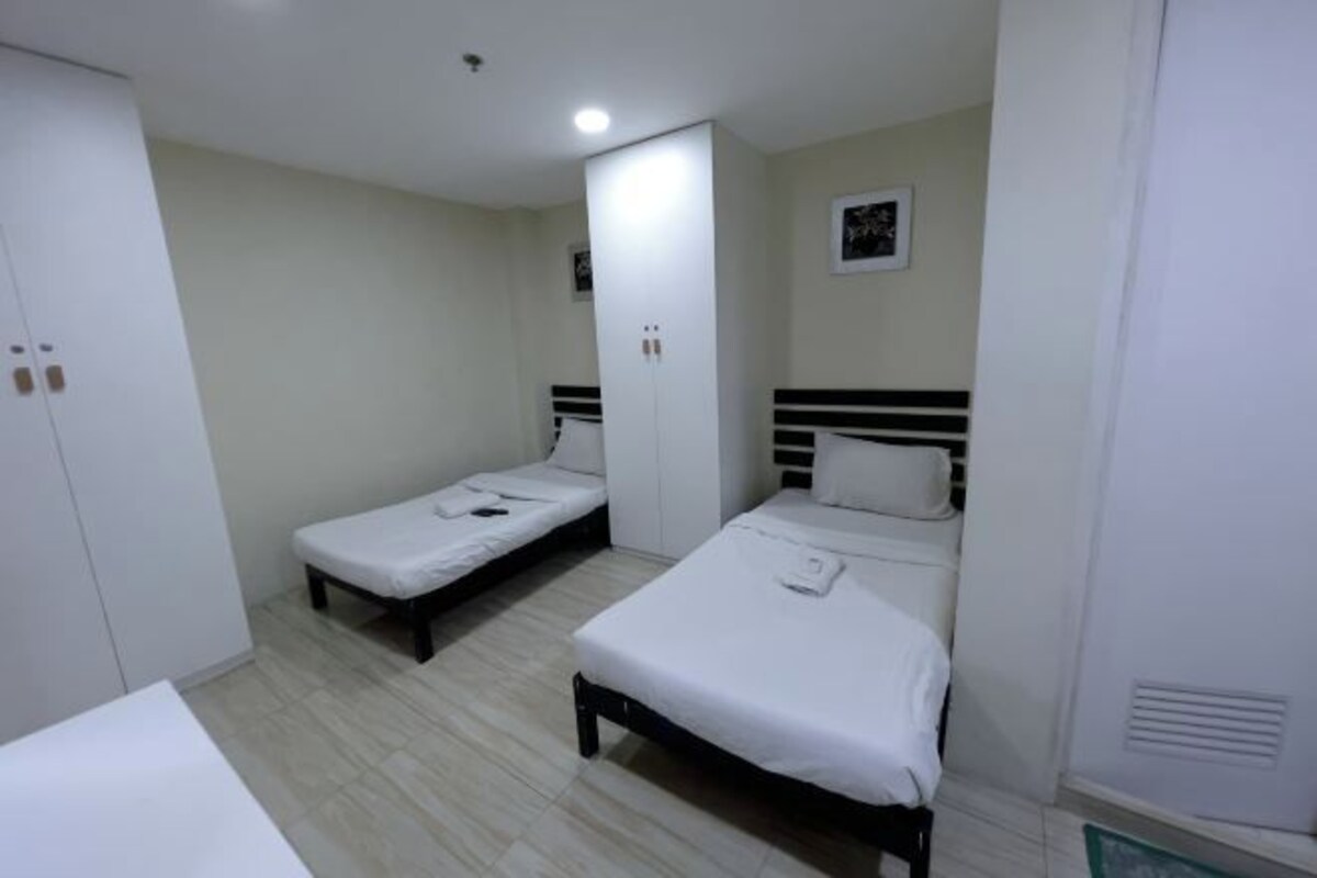 A room with two single beds, a wardrobe, and a small bedside table.