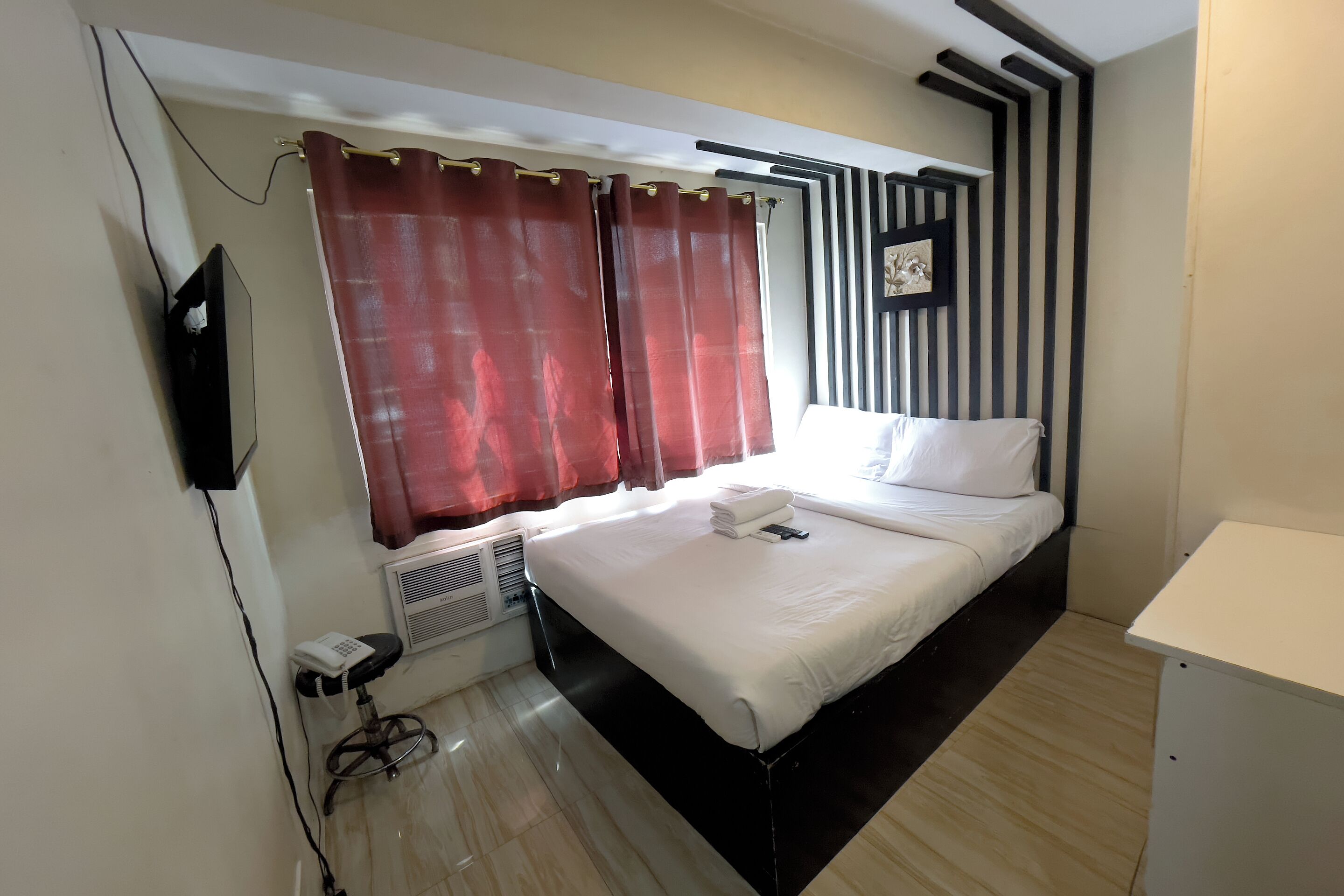 A hotel room with a bed, a desk, a chair, a TV, and a window with curtains.