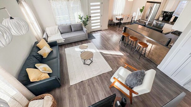 Ein modernes Wohnzimmer mit Sofa, Couchtisch und Fernseher. Es gibt eine Küchenzeile mit Esstisch und Stühlen.