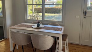 Un'area pranzo con tavolo, due sedie, un vaso con bacche rosse e una finestra vista giardino e casa.