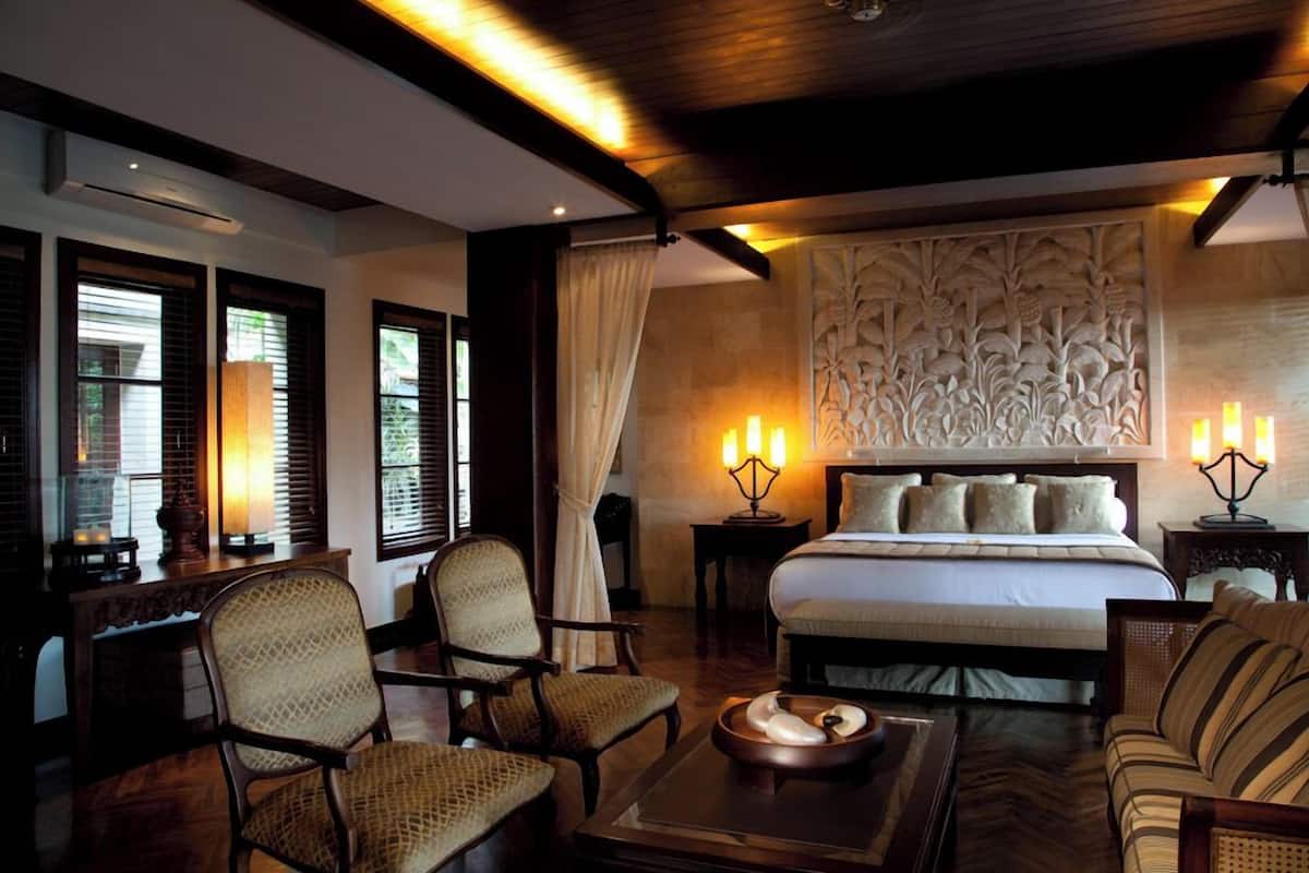 A hotel room with a large bed, two bedside tables with lamps, a sofa, and two chairs.