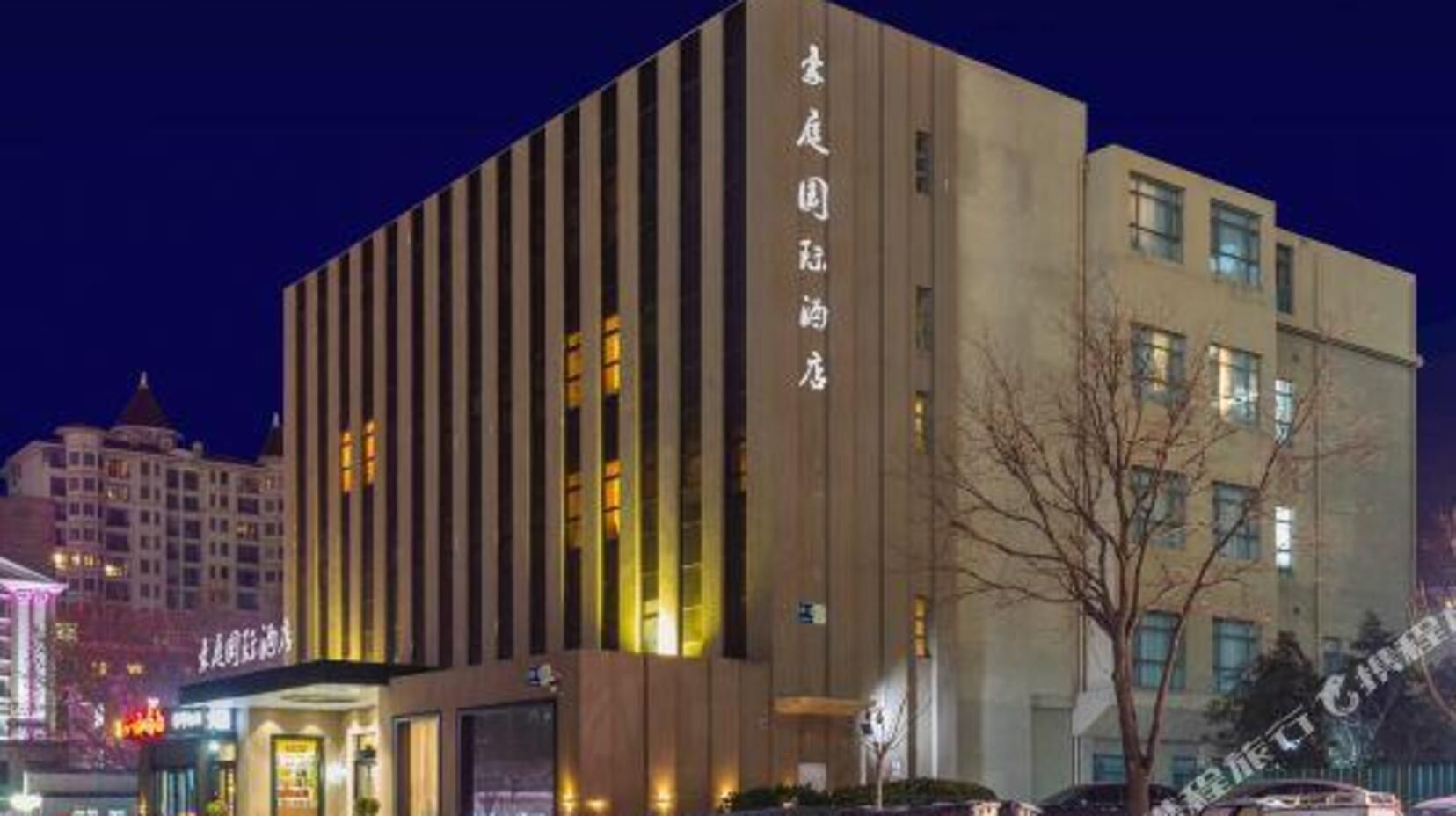 A multi-story hotel with vertical lines on the facade, illuminated windows, and a visible sign with Chinese characters.