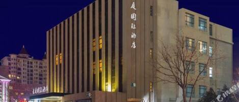 Ein mehrstöckiges Hotel mit vertikalen Linien an der Fassade, beleuchteten Fenstern und einem Schild mit chinesischen Schriftzeichen.