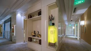 A hotel corridor with a white reception desk, a glass display case with decorative items, and a patterned carpet. - Haoting International Hotel (Beijing)