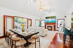A spacious living room with a fireplace, a dining area with a large table and chairs, and a television mounted on the wall.