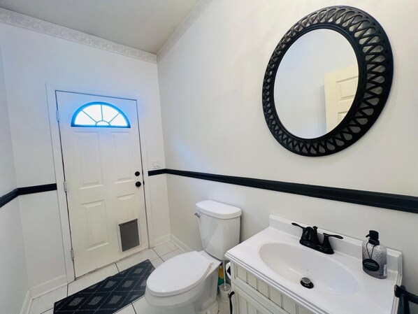 A bathroom with a white toilet, a white sink, a black-framed mirror, and a door with a blue-lit window.