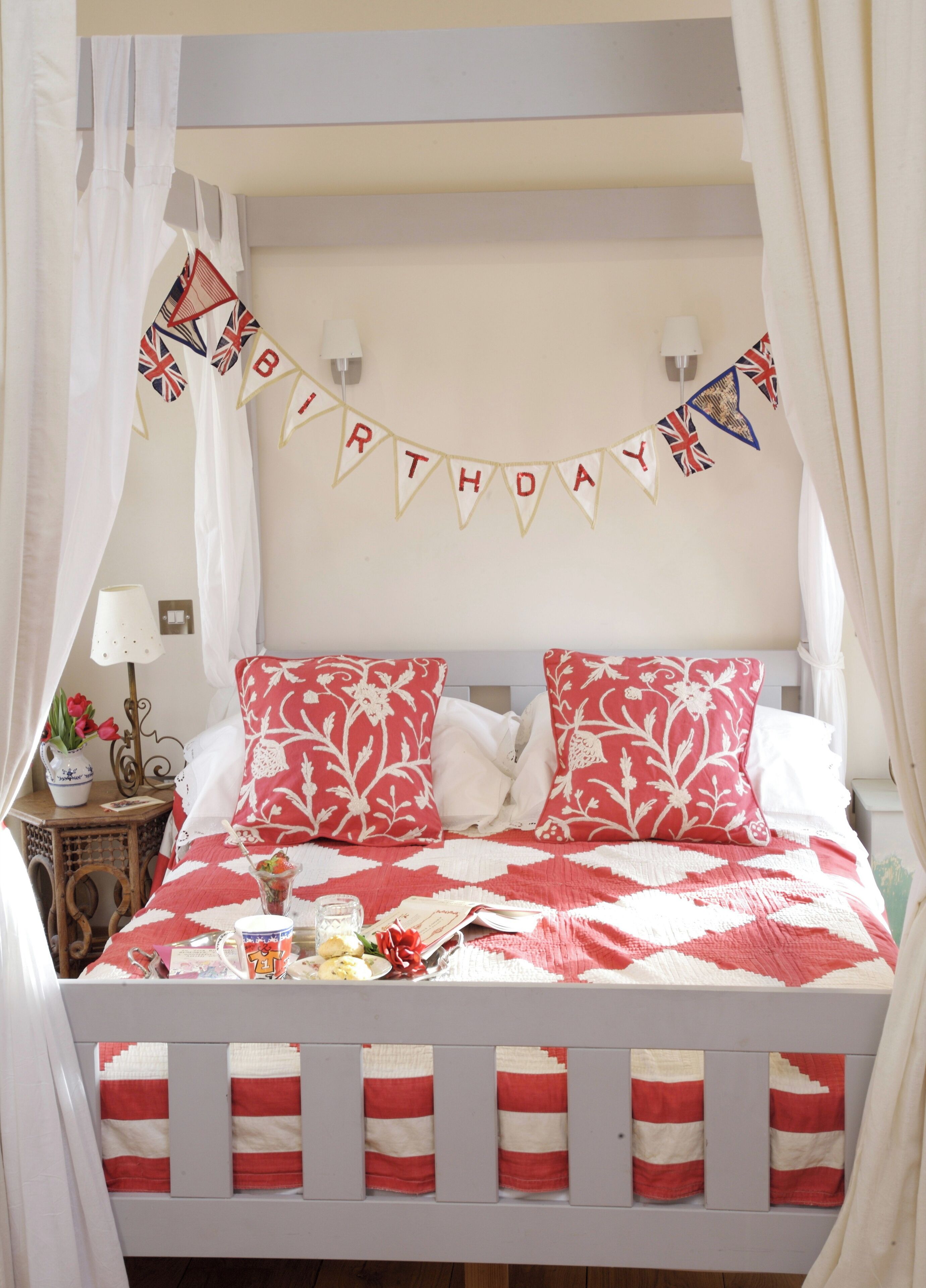 A bed with a red and white checkered bedspread, a 'BIRTHDAY' banner, and floral pillows.
