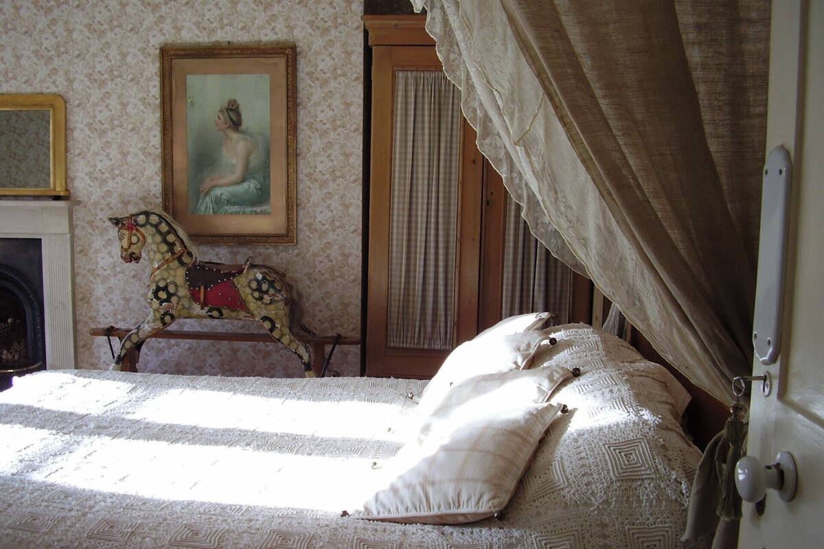 Een slaapkamer met een bed met een geruit sprei, een schommelpaard, een schilderij aan de muur en een raam met gordijnen.
