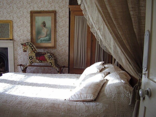 A bedroom with a patterned bedspread, a rocking horse, a painting on the wall, and a window with curtains. - Fosse Farmhouse B&B and Holiday Cottages (Chippenham)