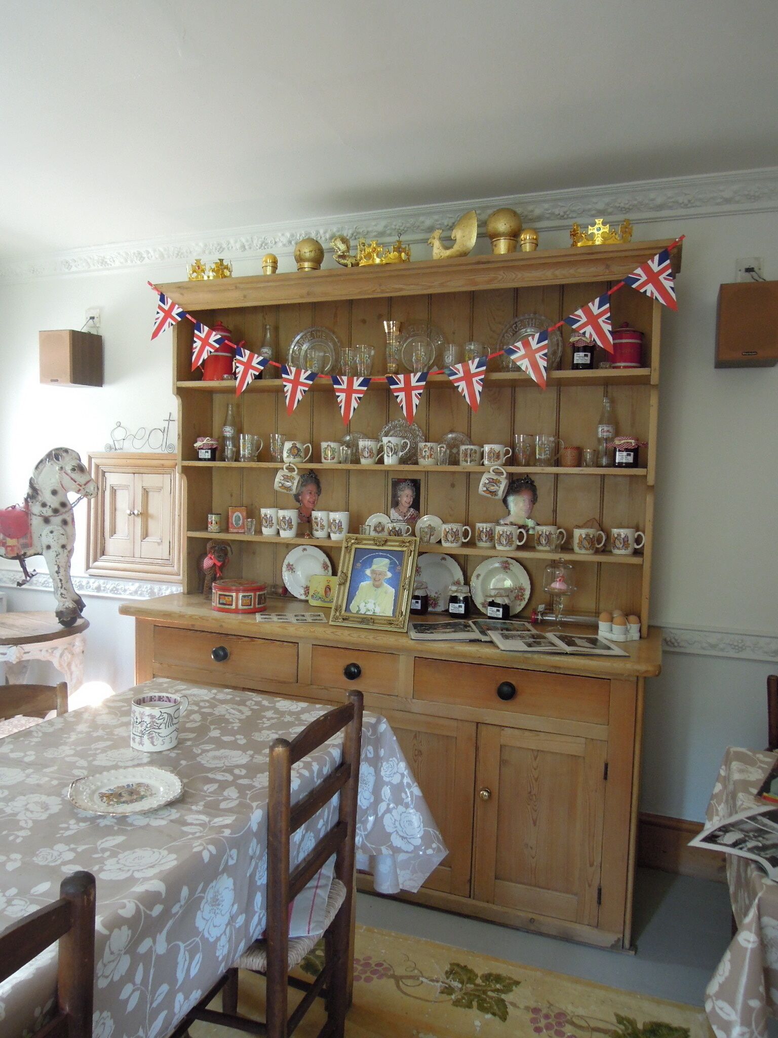 A dining area with a wooden buffet table, chairs, and a wall-mounted display of dishes and glasses.