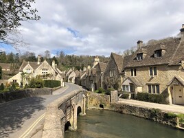 A stone bridge over a river, leading to a row of traditional stone houses with pitched roofs.
