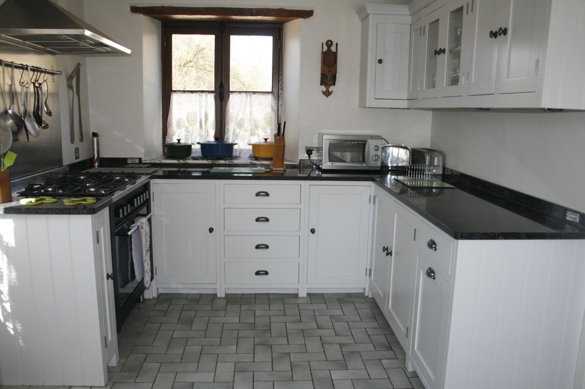 A kitchen with white cabinets, a stove, a microwave, and a window with curtains.