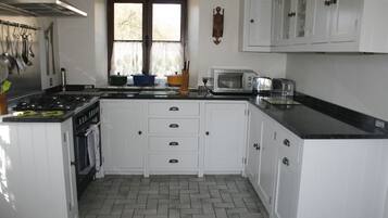 A kitchen with white cabinets, a stove, a microwave, and a window with curtains.