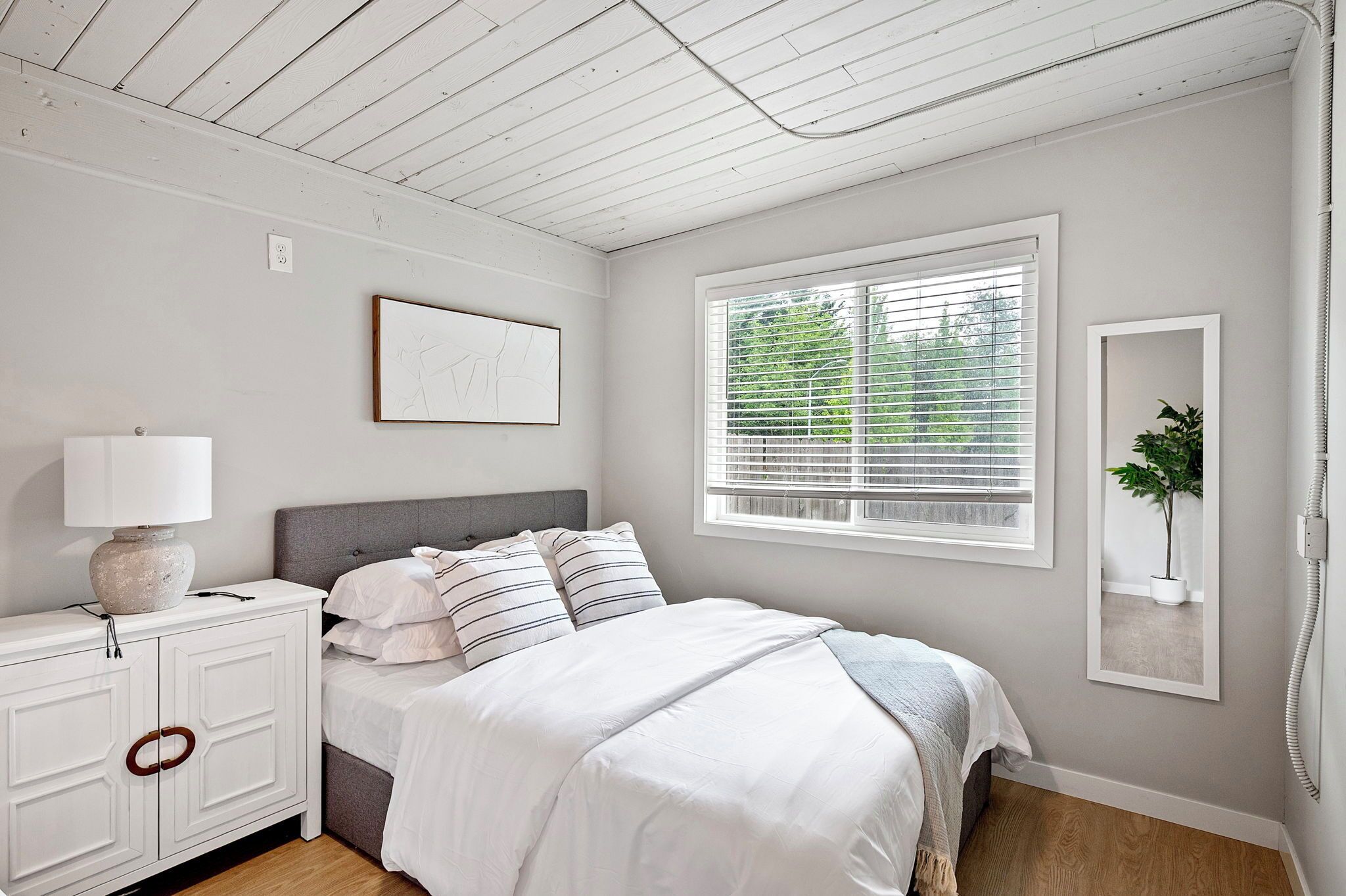 A bedroom with a bed, bedside table, lamp, and a window with blinds.