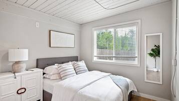 A bedroom with a bed, bedside table, lamp, and a window with blinds.