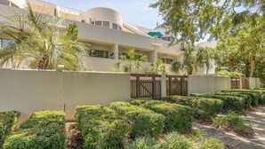A modern building with a curved facade, a gated entrance, and well-maintained hedges.