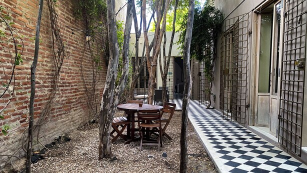 Un patio con suelo a cuadros, una mesa de madera con sillas y un muro de ladrillo.