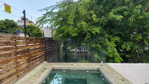 Una piscina rectangular con baldosas de piedra, rodeada por una valla de madera y paneles de vidrio, con árboles al fondo.