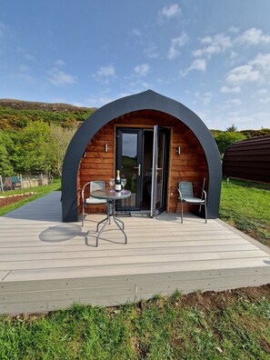 Una estructura de madera arqueada moderna con un patio, dos sillas, una mesa y una botella de vino.