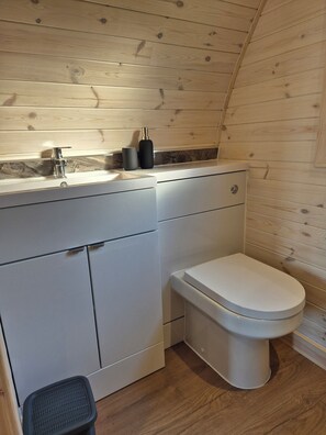 A compact bathroom with a wooden wall, a white toilet, and a sink with a marble backsplash.