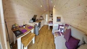Un interior de cabaña acogedor con detalles de madera, un comedor, un sofá y una pequeña cocina.