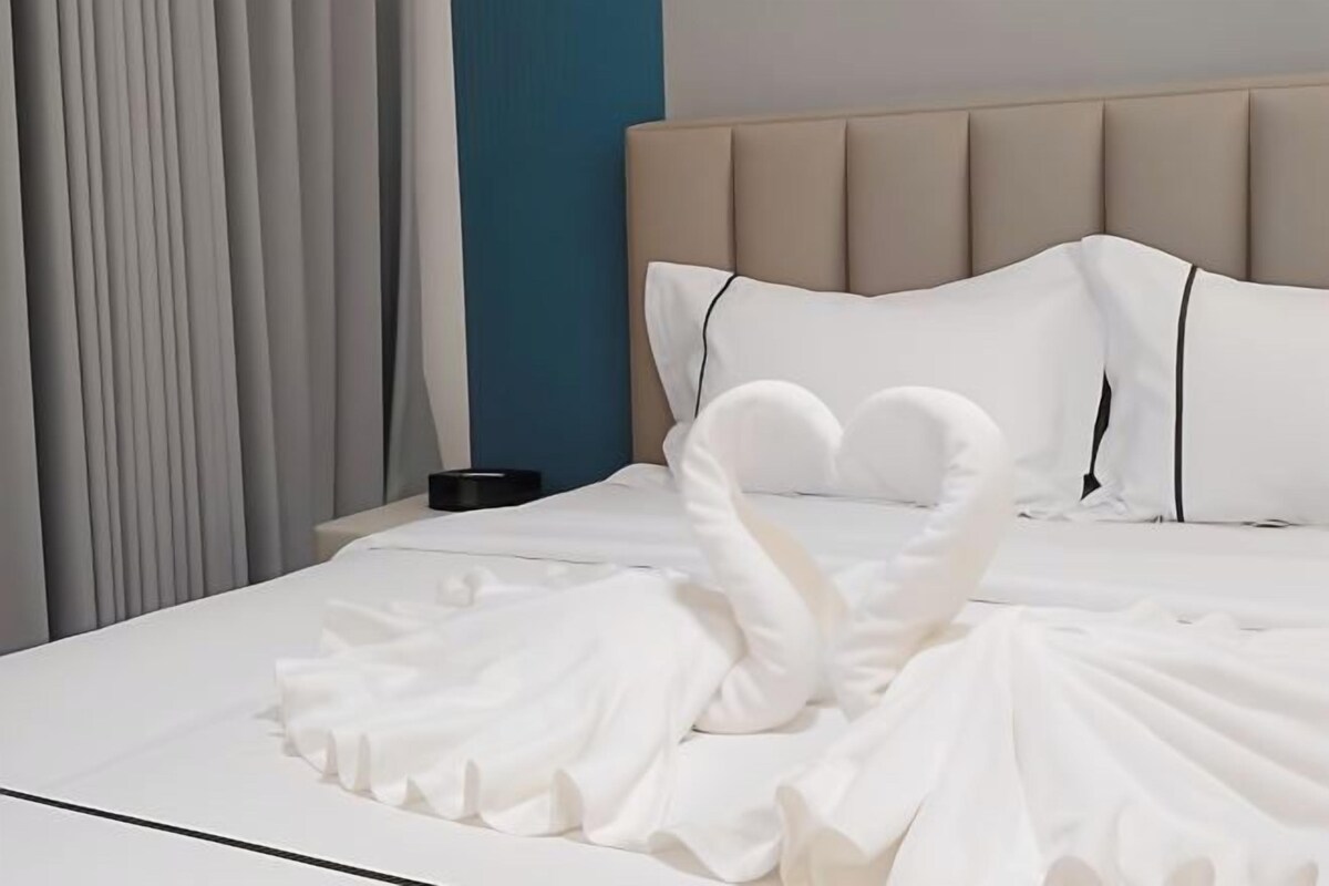 A neatly made bed with white linens and a decorative swan pillow arrangement.