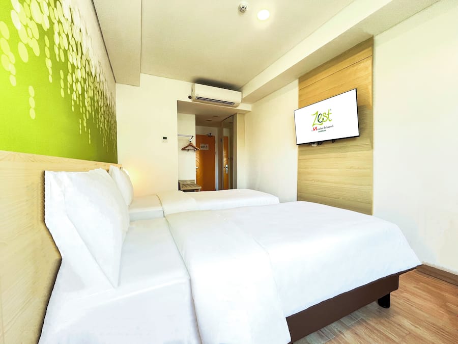 Quarto de hotel com uma cama, uma TV fixada na parede e uma porta que dá para um banheiro.