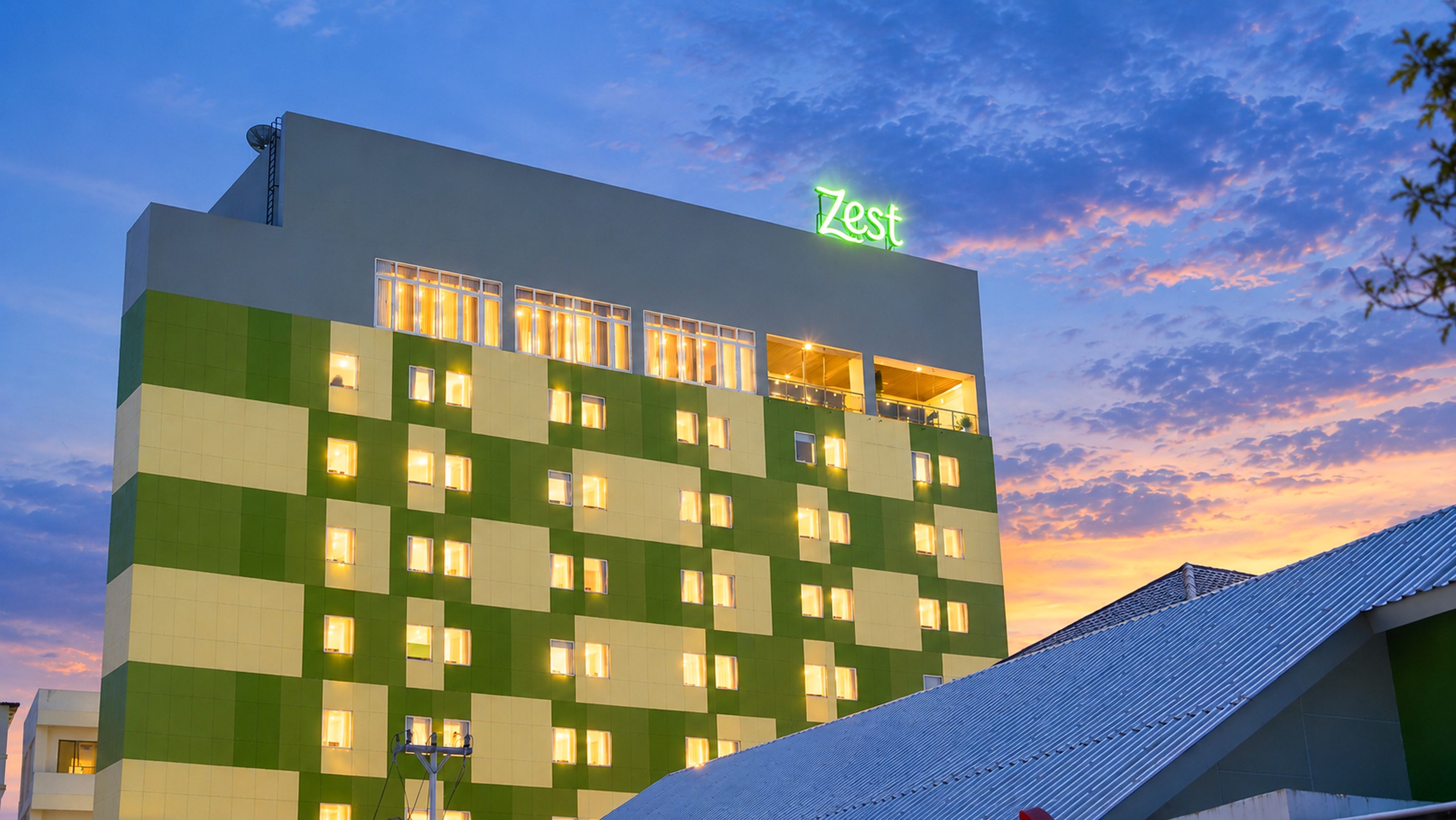 Un hotel con fachada verde y blanca, varias ventanas y un letrero de neón en la parte superior.