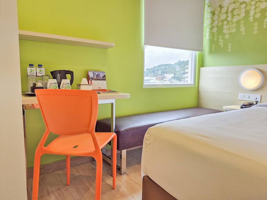 Una habitación de hotel con cama, escritorio y silla, ventana con vistas y mesita de noche con lámpara.