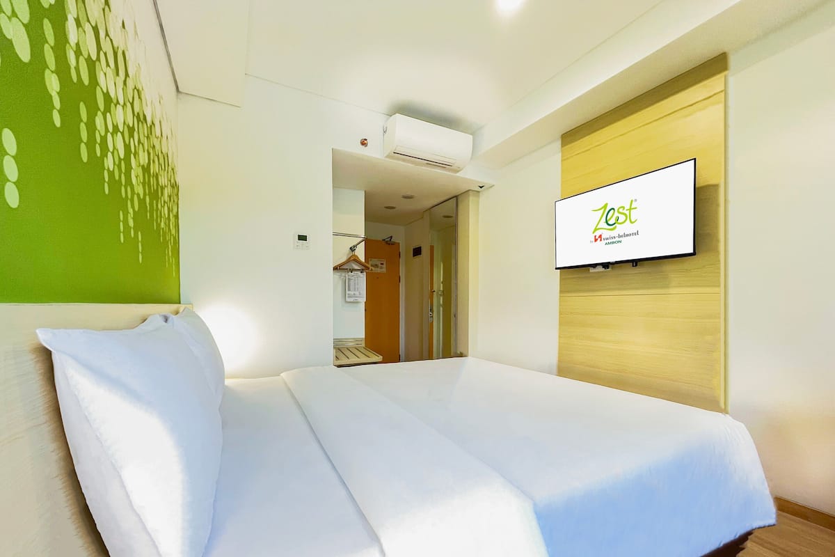 A hotel room with a bed, a television mounted on the wall, and a green wall decoration.