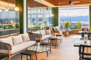 A rooftop bar with outdoor seating, including sofas and tables, overlooking a cityscape with mountains in the distance. - Zest Ambon by Swiss-Belhotel International (Ambon)