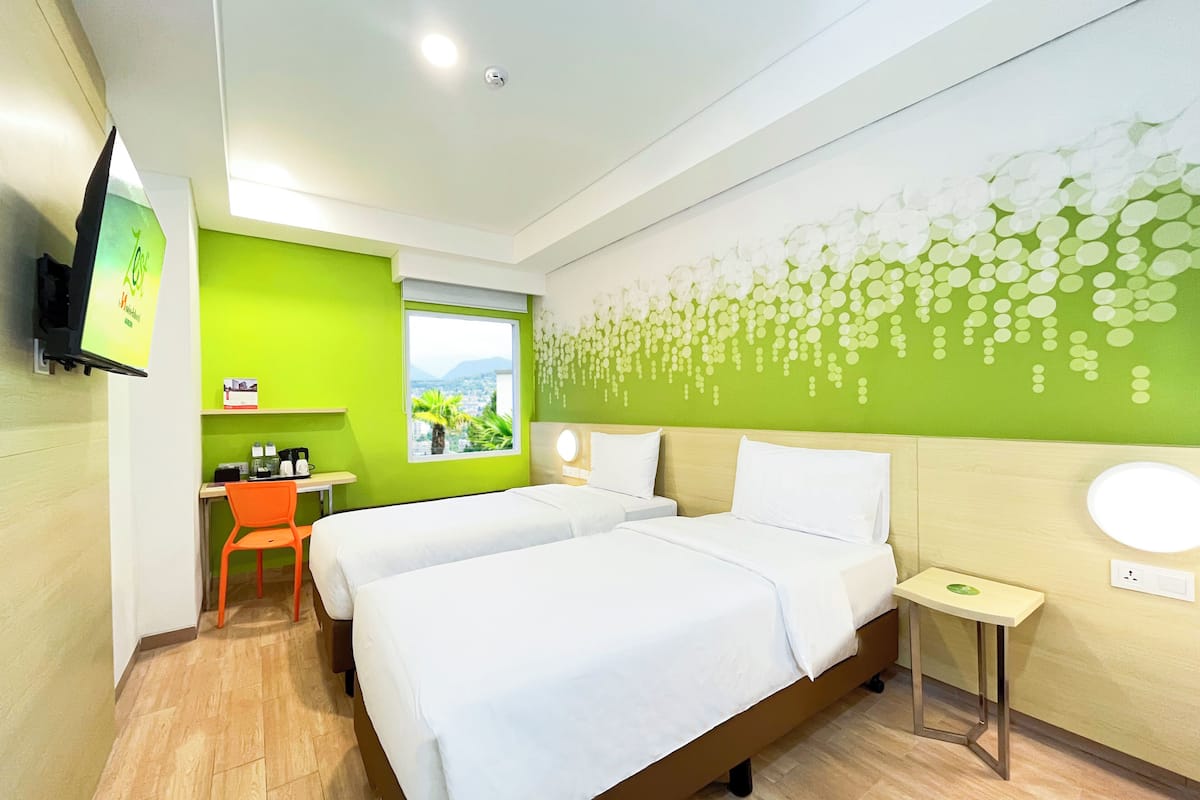 A hotel room with two beds, a desk, and a window with a view.