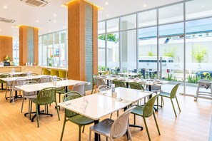A spacious indoor dining area with multiple tables and chairs, large windows offering a view of the outside, and a reception desk. - Zest Ambon by Swiss-Belhotel International (Ambon)