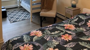 Een slaapkamer met stapelbed, een bed met een patroon, een stoel, een klein tafeltje met lamp en twee decoraties aan de muur.