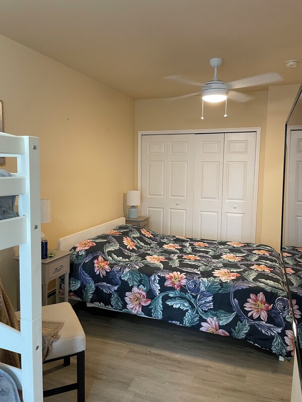 Un dormitorio con cama, ventilador de techo, armario y mesita de noche con lámpara.
