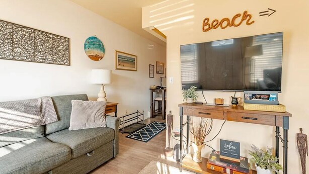 Een woonkamer met een bank, een televisie op een dressoir, een kunstwerk aan de muur en een bord met de tekst 'Beach'.
