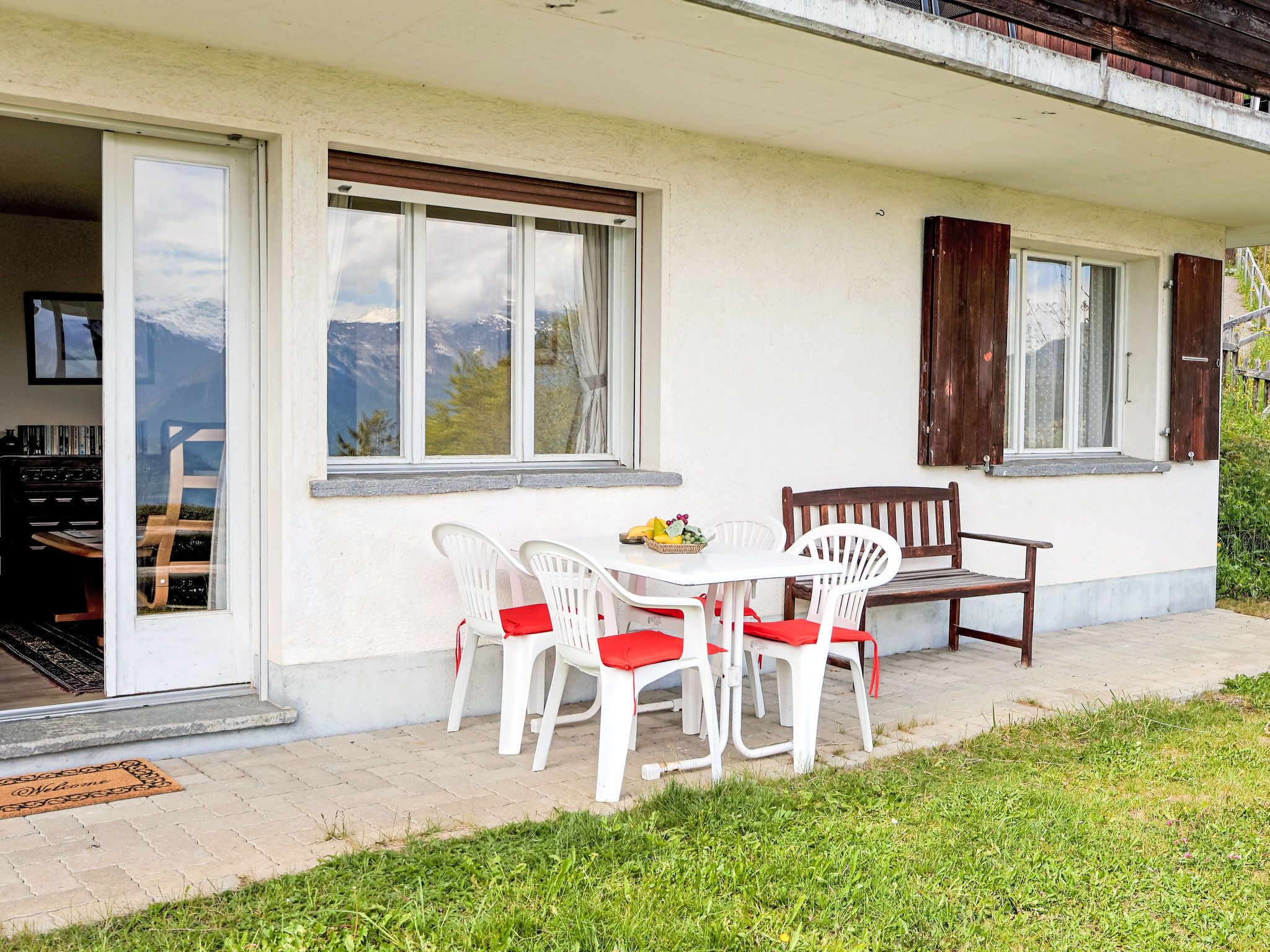 A patio with a table and chairs, a wooden bench, and a view of mountains through the windows.