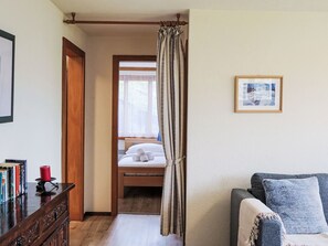 Una camera d'albergo con un letto di legno, un comodino con libri, una candela rossa, una tenda grigia, un quadro appeso al muro e un divano grigio.